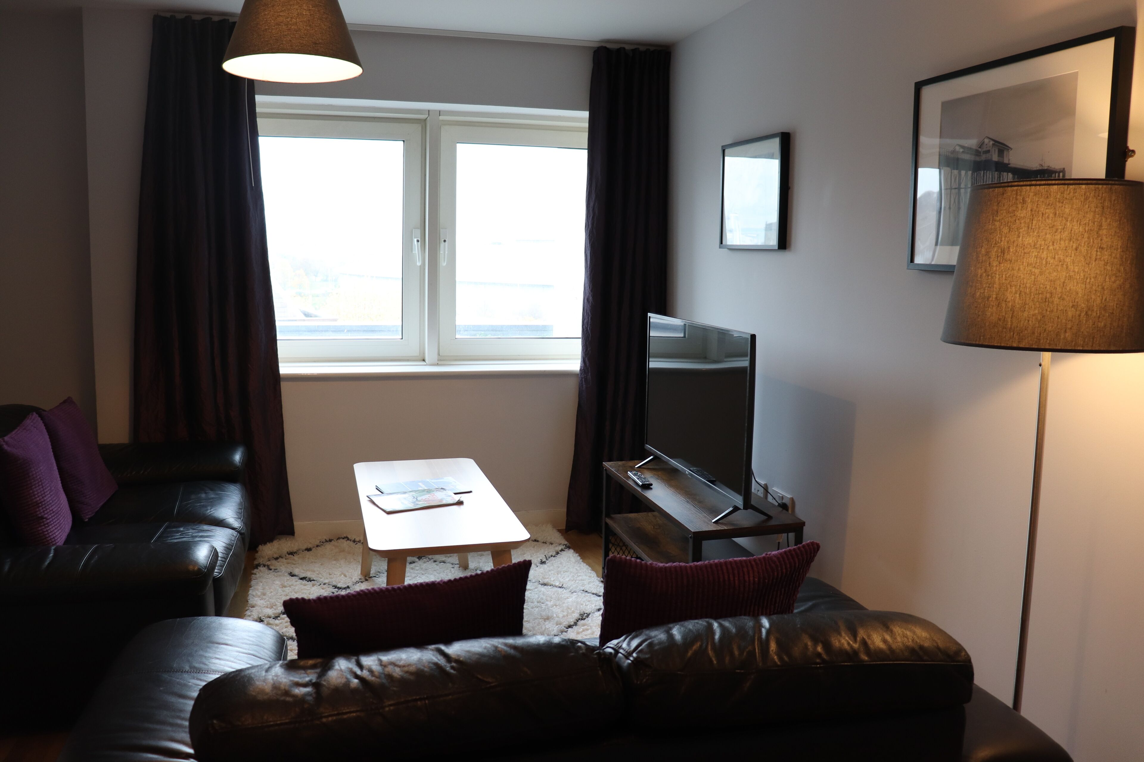 Een moderne woonkamer met een leren bank, een salontafel, een flatscreen televisie en een vloerlamp.