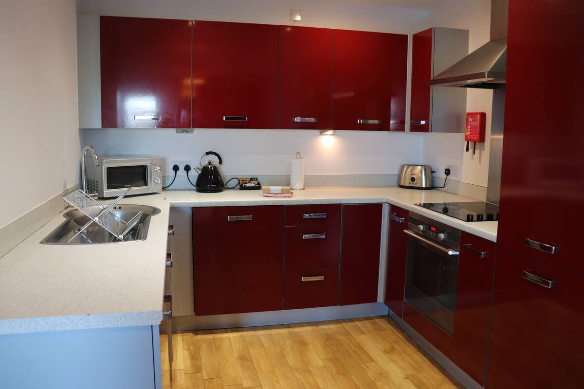 A modern kitchen with red cabinets, a microwave, kettle, toaster, and a built-in oven.