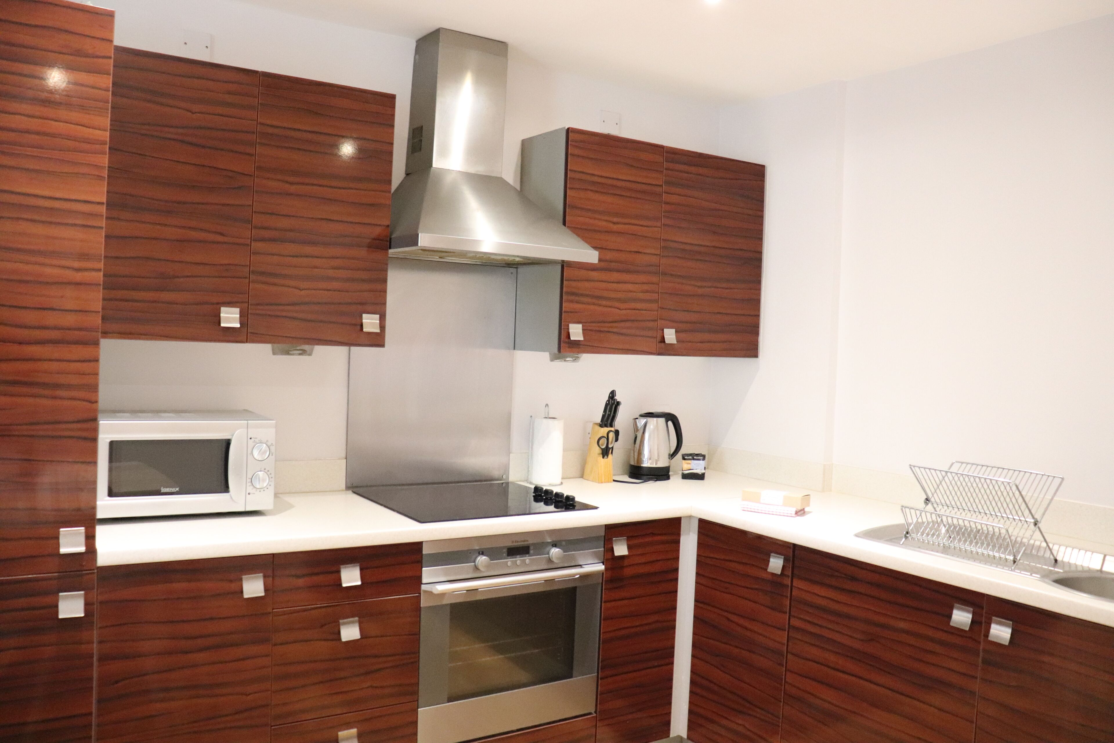 A modern kitchen with wooden cabinets, a stainless steel range hood, a microwave, and a built-in oven.