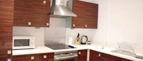 A modern kitchen with wooden cabinets, a stainless steel range hood, a microwave, and a built-in oven.