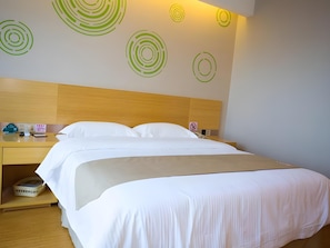 Quarto de hotel com uma cama de casal, cabeceira de madeira, mesa de cabeceira com telefone e uma pequena mesa, e parede com desenhos circulares.