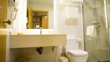 A bathroom with a glass shower enclosure, a toilet, a sink with a mirror, and a telephone.