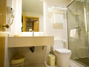 Un baño con cabina de ducha de vidrio, inodoro, lavamanos con espejo y teléfono.