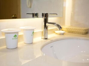 Casa de banho com lavatório branco, torneira cromada e duas chávenas brancas com logótipos verdes.