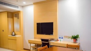 Una habitación de hotel moderna con un escritorio de madera, un televisor de pantalla plana, una mesa de comedor y una planta en maceta.