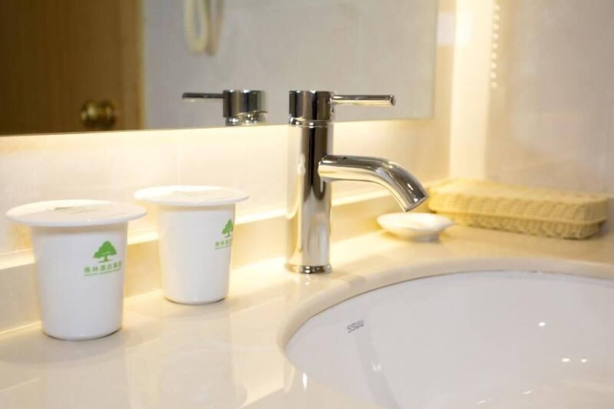 A bathroom with a white sink, two white cups with green logos, and a soap dish.