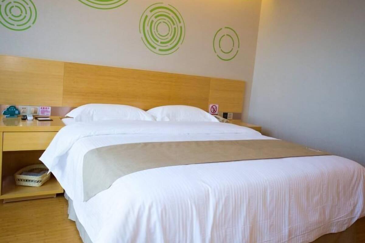 A hotel room with a wooden headboard, a bed with white bedding, and a nightstand with a phone and a sign.
