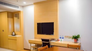 Una habitación de hotel moderna con un escritorio de madera, un televisor de pantalla plana, una mesa de comedor y una planta en maceta.