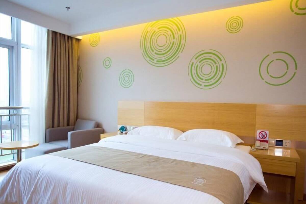 A hotel room with a large bed, a wooden headboard, a bedside table with a phone, and a wall with circular patterns.
