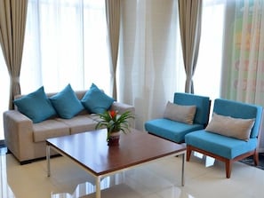 A living room with a beige sofa, two blue armchairs, a wooden coffee table, and a potted plant. - Greentree Inn Suzhou Changshu Huanghe Road Linli C (Suzhou)