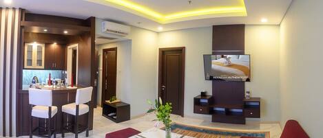 A modern living room with a TV, seating, a kitchen area, and a dining space.