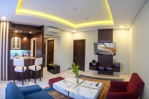 A modern living room with a TV, seating, a kitchen area, and a dining space.