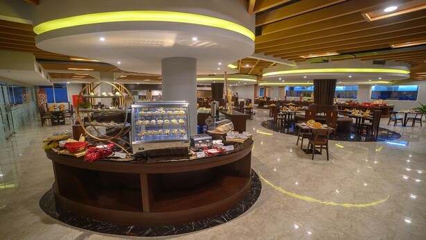 Un vestíbulo de hotel con una zona de exhibición de alimentos en el centro, áreas de descanso y un diseño de techo moderno.