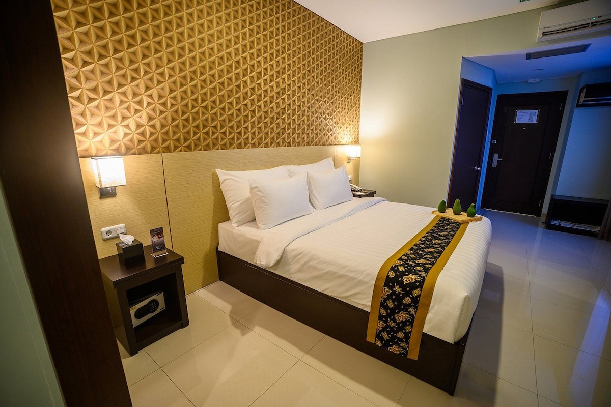 Una habitación de hotel con cama, mesita de noche, lámpara y un papel tapiz estampado.