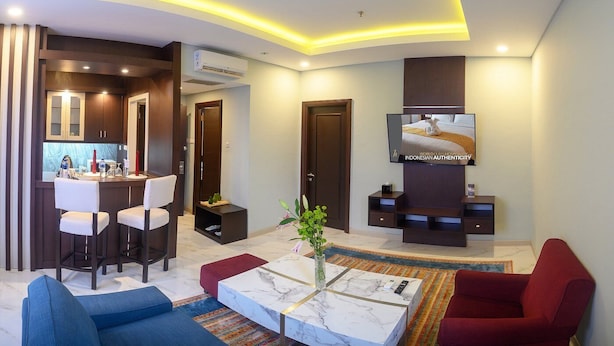 A modern living room with a TV, seating, a kitchen area, and a dining space.