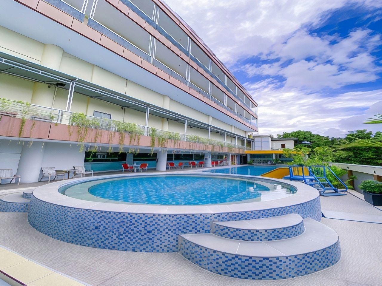 Una piscina con plataforma de baldosas, rodeada por un edificio de varios pisos con balcones.