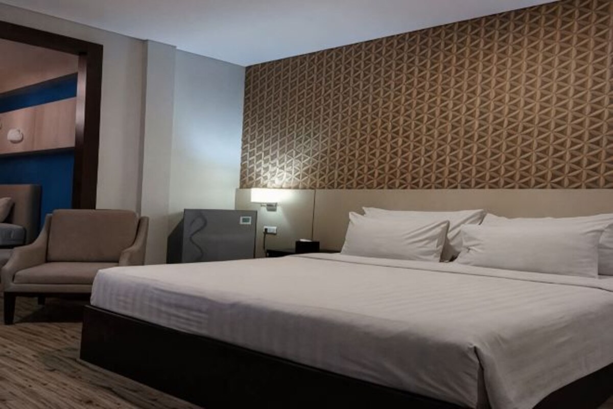 Une chambre d’hôtel avec un grand lit, une chaise, un bureau et une tête de lit à motifs.