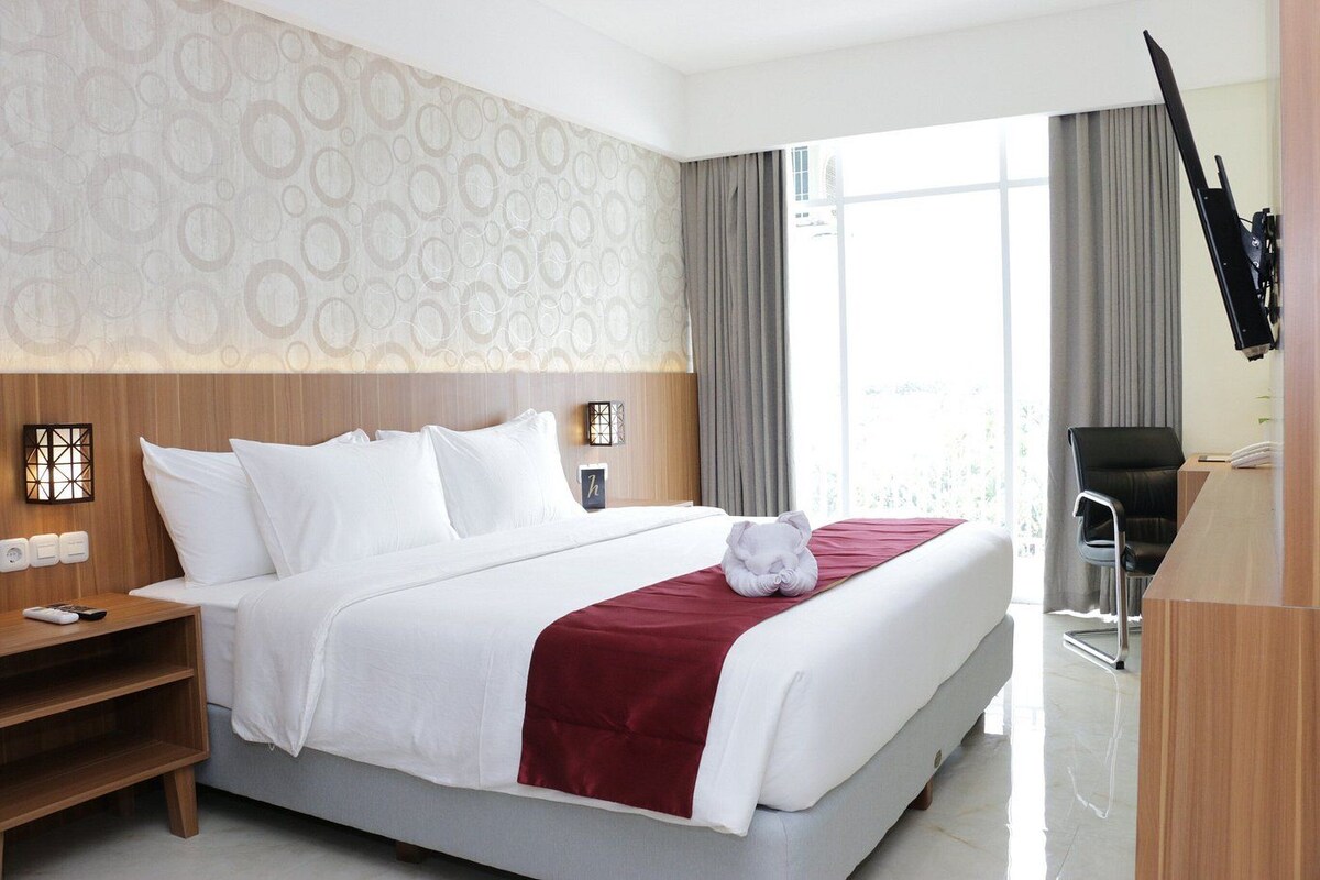 Una habitación de hotel con cama, mesita de noche, lámpara y escritorio con silla.
