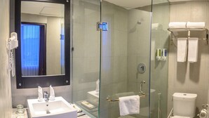 Un baño moderno con ducha de vidrio, un espejo grande, un lavamanos blanco y un inodoro.