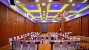 Un salón de conferencias con largas mesas, sillas blancas y piso alfombrado.