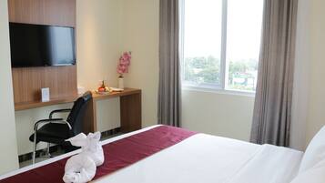 A hotel room with a bed, a desk with a chair, a television, and a window with curtains.