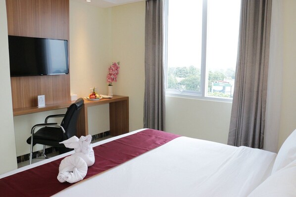 A hotel room with a bed, a desk with a chair, a television, and a window with curtains. - Horison Kotaraja Papua (Sentani)