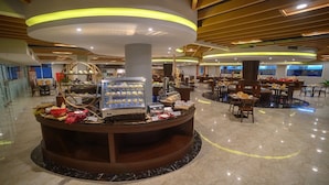 A hotel lobby with a central food display, seating areas, and a modern ceiling design.