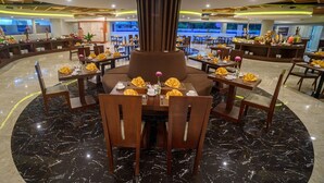 Un restaurante con una zona de estar central, varias mesas de comedor y suelo de mármol.