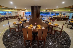 Ein Restaurant mit einem zentralen Sitzbereich, mehreren Esstischen und einem Marmorboden.