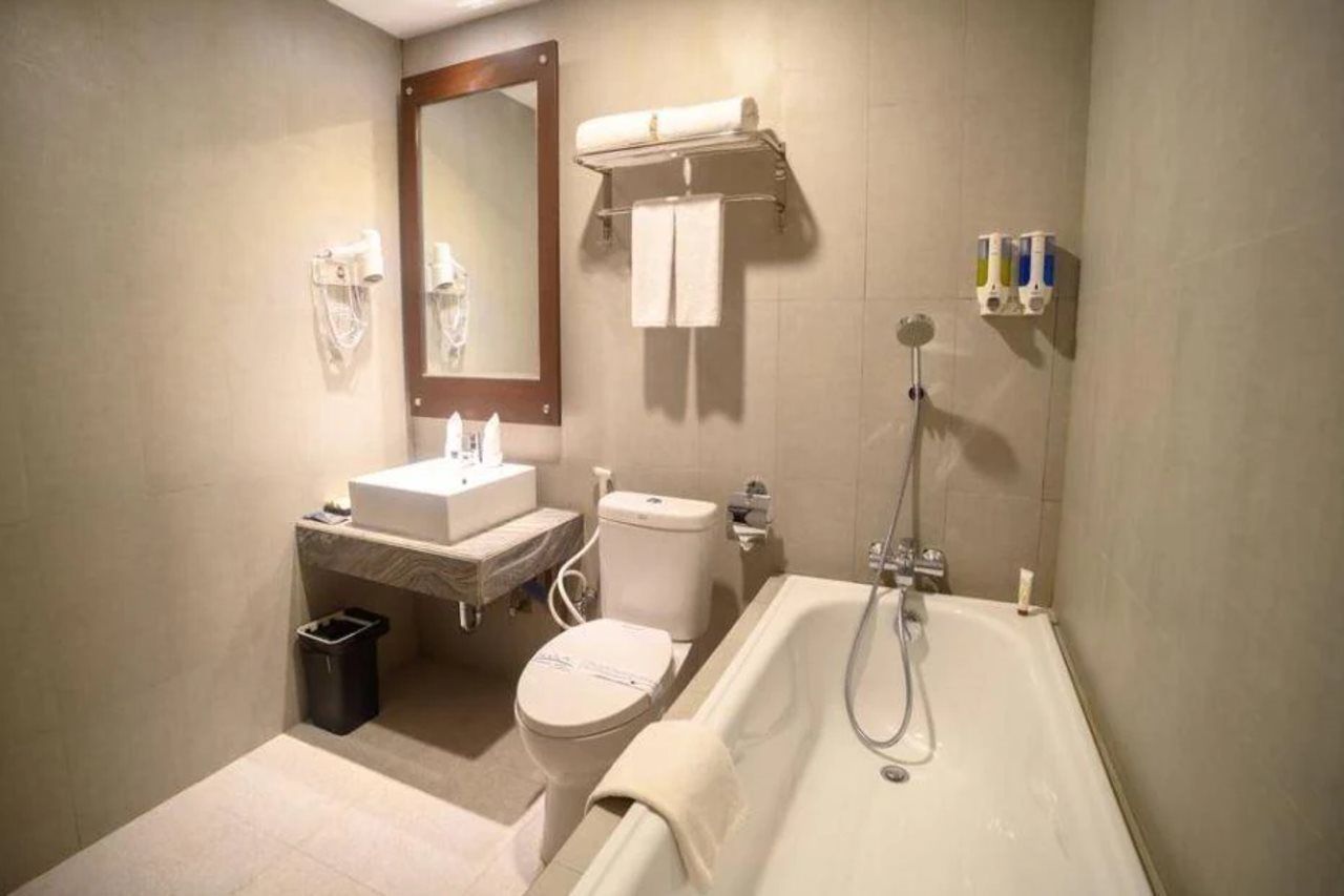 Een badkamer met toilet, wastafel, spiegel, handdoekrek en bad.