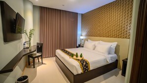 A modern hotel room with a large bed, a desk with a chair, a TV mounted on the wall, and a patterned wall.