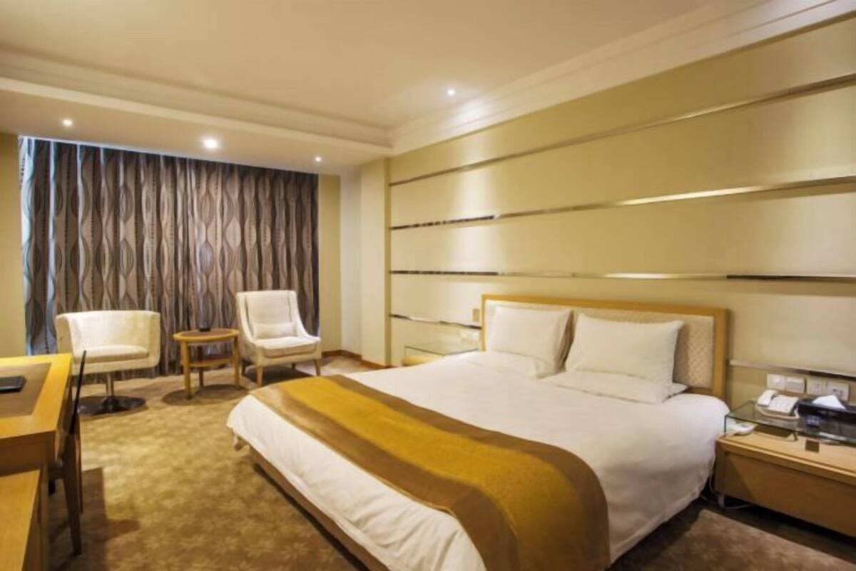Une chambre d’hôtel avec un grand lit, un bureau, une chaise, une petite table et un rideau.