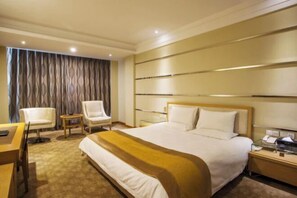 Una camera d'albergo con un letto grande, una scrivania, una sedia, un tavolino e una tenda.