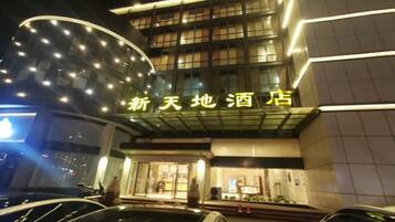 A hotel with a modern facade, illuminated signage, and a parking area with cars.