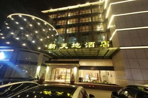 Un hotel con fachada moderna, señalización iluminada y un estacionamiento con automóviles.