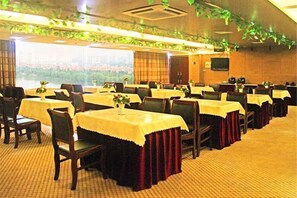 Un salón de banquetes con mesas dispuestas en filas, cada una con mantel y un jarrón de flores.
