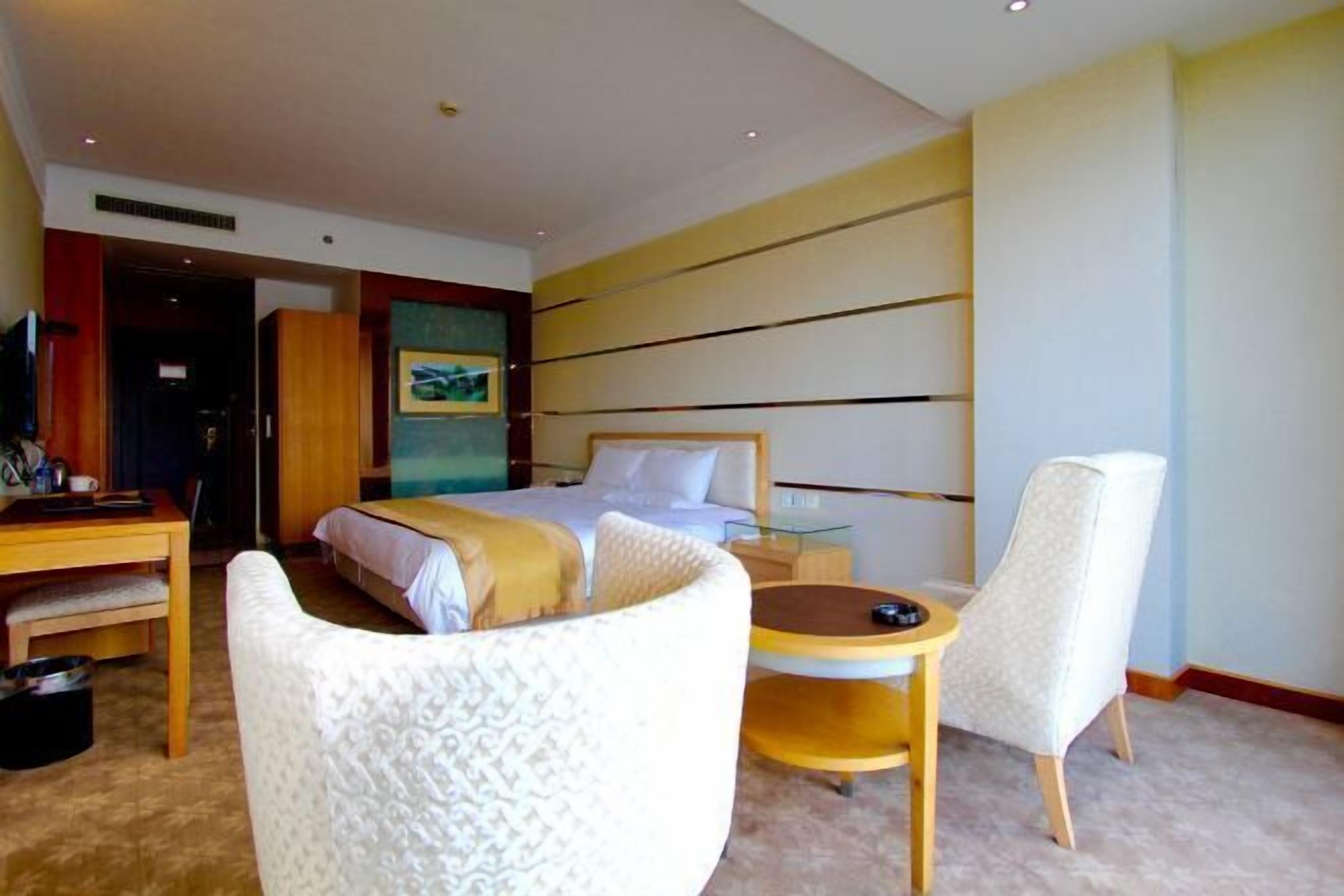 A hotel room with a bed, a desk, a chair, and a small table.