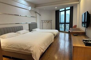Habitación de hotel con dos camas, un escritorio, una silla, un televisor y un ventanal con vista a la ciudad.