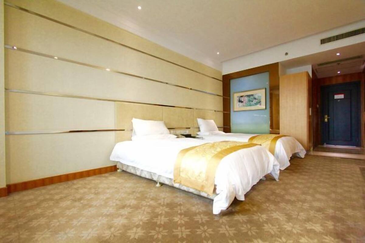 Une chambre d’hôtel avec deux lits, une grande fenêtre et une porte donnant sur un couloir.