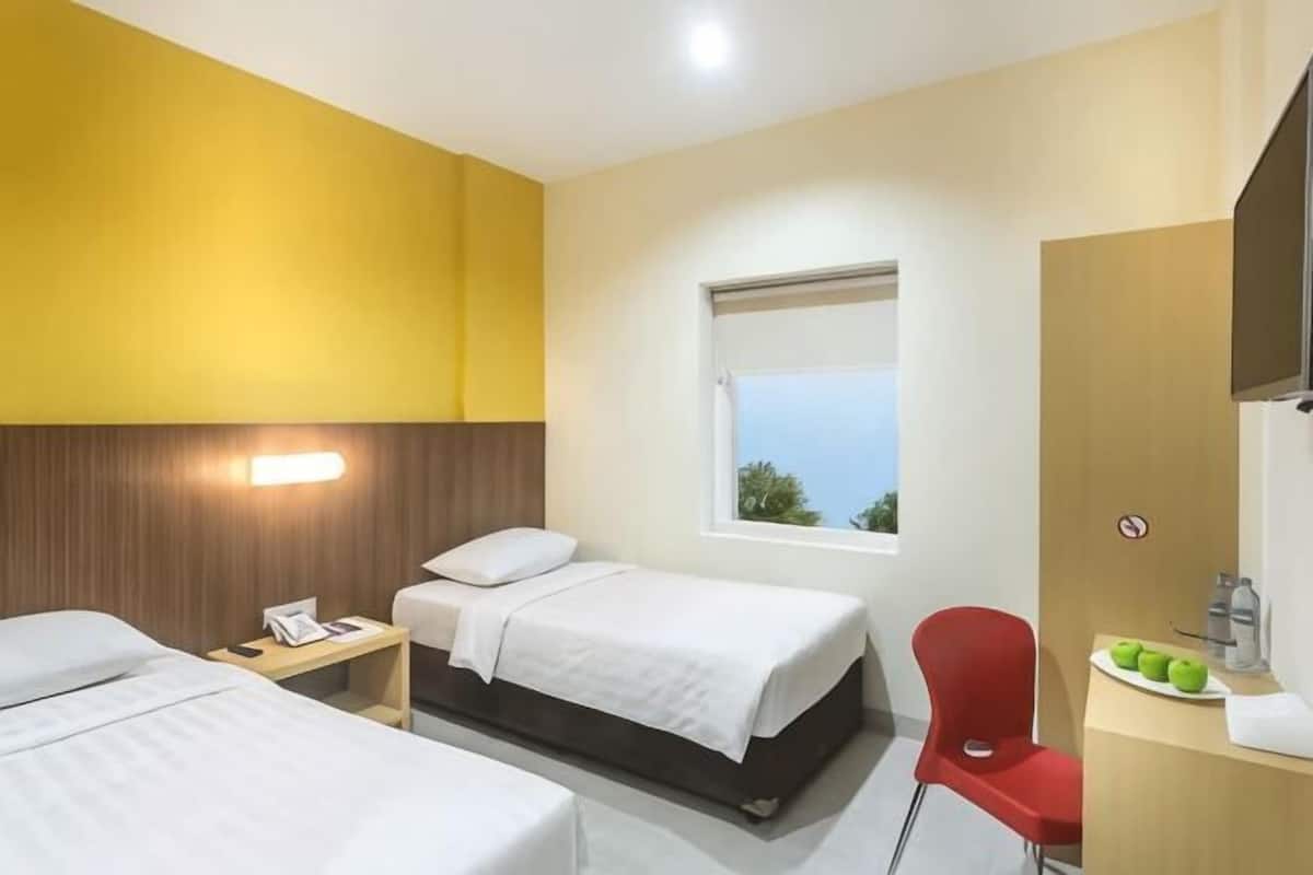 A hotel room with two beds, a desk with a chair, a window, and a bathroom mirror.