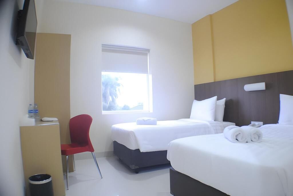 A hotel room with two beds, a desk, a chair, a TV, and a window.