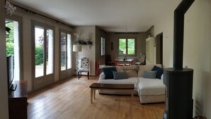 Un salon spacieux avec un canapé, une table basse et une cheminée. De grandes fenêtres offrent une vue sur la verdure environnante.