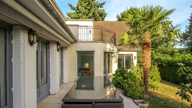 Une maison moderne dotée d’un patio en verre, d’un balcon et d’un jardin bien entretenu.