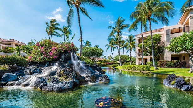 A resort with a clear pool, palm trees, and a waterfall. - 🏖️Golf Course Views + Large Lanai | Shores #202 (Waikoloa)