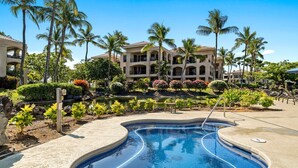A swimming pool with a curved design, surrounded by palm trees and a building with multiple balconies. - 🏖️Golf Course Views + Large Lanai | Shores #202 (Waikoloa)