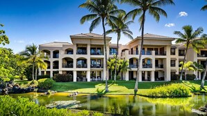 A multi-story hotel with balconies, a landscaped garden, and a pond. - 🏖️Golf Course Views + Large Lanai | Shores #202 (Waikoloa)