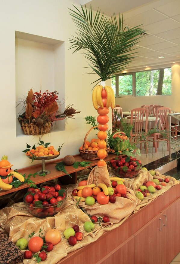 A buffet table with various fruits and vegetables, a decorative palm plant, and a wall-mounted plant arrangement.
