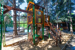 Un parque infantil con una estructura de madera para escalar, un tobogán y un pequeño refugio.