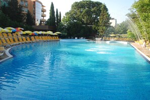 Una piscina con sillas de descanso amarillas y sombrillas, rodeada de árboles y edificios.