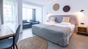 A modern hotel room with a large bed, a seating area with a table, and a view through the window. - Hotel Excelsior (Golden Sands)